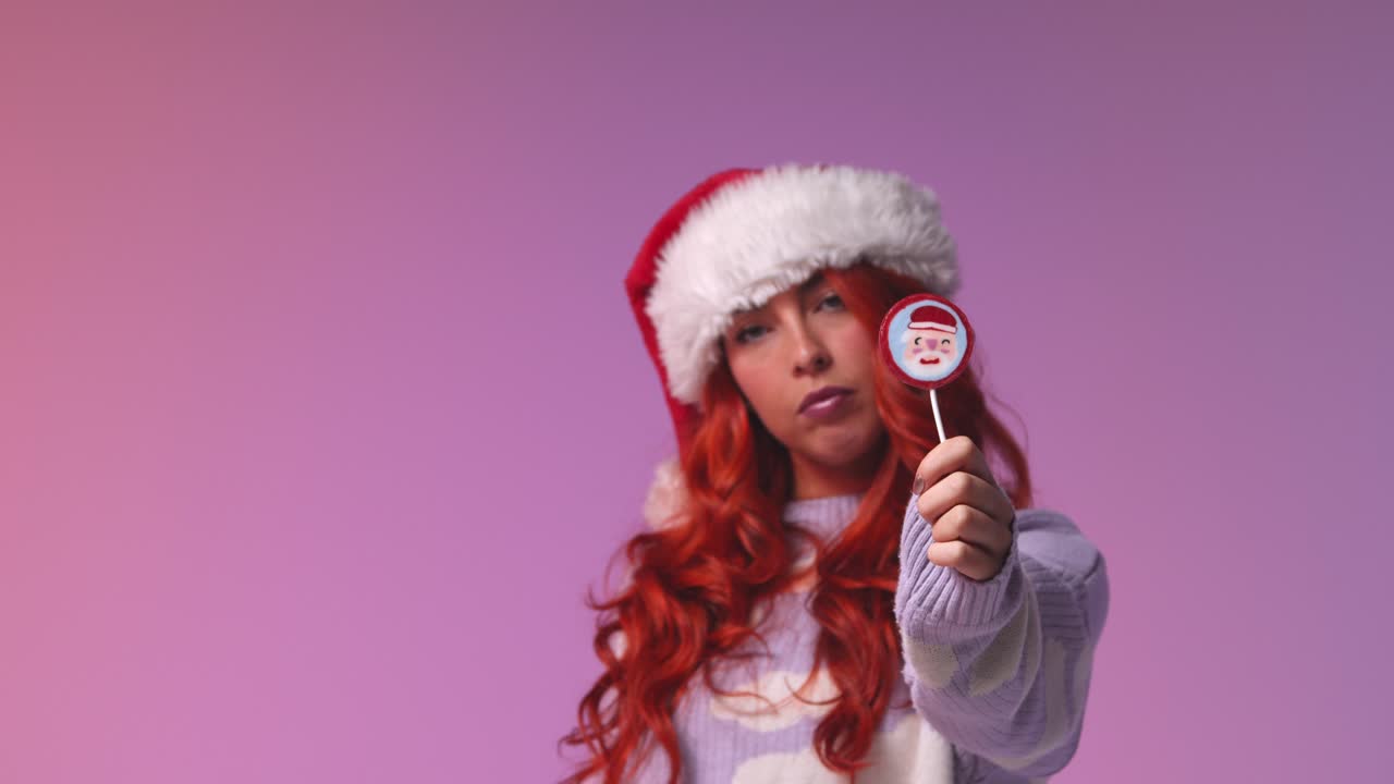 retrato de estudio de una mujer joven de la generación z con un sombrero de papá noel sosteniendo una piruleta de caramelo