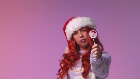 Studio-Portrait-Shot-Of-Young-Gen-Z-Woman-Wearing-Christmas-Santa-Hat-Holding-Candy-Lollipop