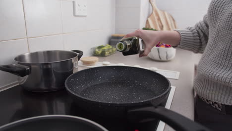 woman hands pouring olive oil into frying pan before cooking