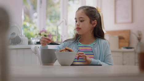 niña feliz usando una tableta comiendo galletas sumergiendo galletas en chocolate caliente disfrutando de la navegación en línea relajándose en casa