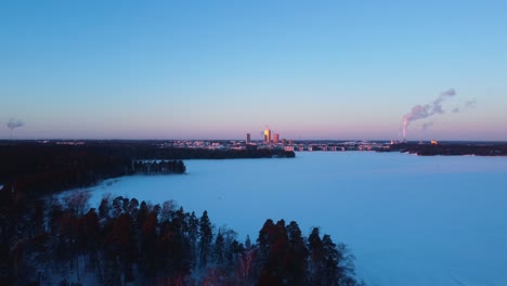 drone shot over snowy ice with sunlit helsinki kalasatama skyline background