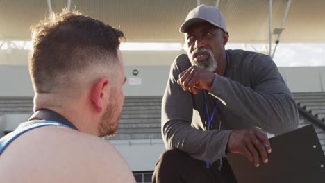 African-american-male-coach-and-caucasian-male-athlete-sitting-and-talking