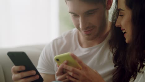 Pareja-Feliz-Usando-Teléfonos-Móviles-Juntos-En-Casa.-Pareja-Mirando-Teléfonos-Móviles