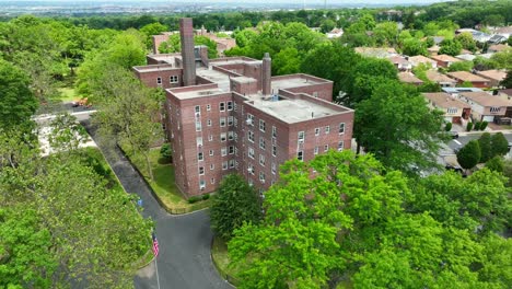 aerial orbiting shot of american apartment block complex surrounded by green trees during sunny day