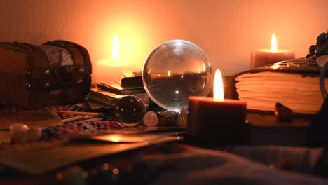 Background of a fortune teller table covered with fabric, with crystal balls, stones, matches, cards, ancient books, rings and candles with flickering flames