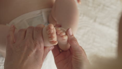 newborn baby feet and toes, mom massages with both hands, white bedsheets