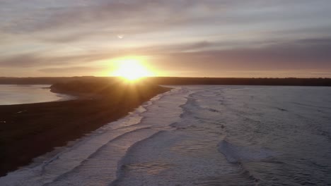 sand dune beach aerial into colourful sunrise, waves roll onto shore