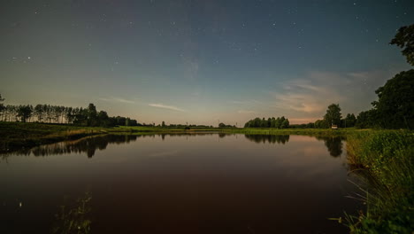 lapso de tiempo de las estrellas en el cielo estrellado que se refleja sobre la superficie del agua del lago al amanecer y los faros de los camiones que conducen a lo largo de la orilla del río o del lago