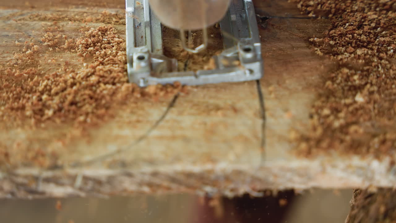 Closeup jigsaw following marked line, carpentry workflow in busy workshop, steady downward cut producing dense sawdust, measured layout lines on board, repetitive precise motion for joinery and fit