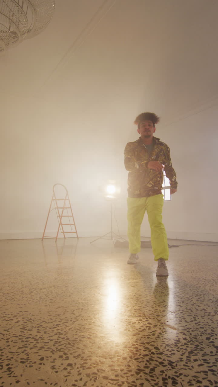 Vertical video of portrait of happy biracial male dancer dancing in dance studio