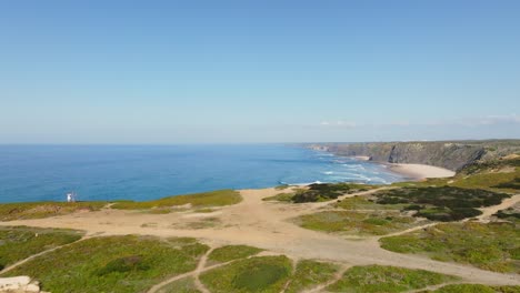 drone flying over the old ruins of ponta da atalaia and rising over to show the beautiful shore where the azure sea meets the coastline of portugal and its majestic high cliffs