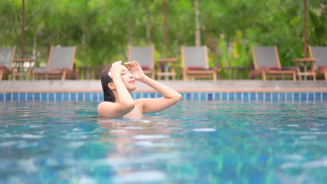 young asian beautiful woman inside pool water sensually strokes wet hair