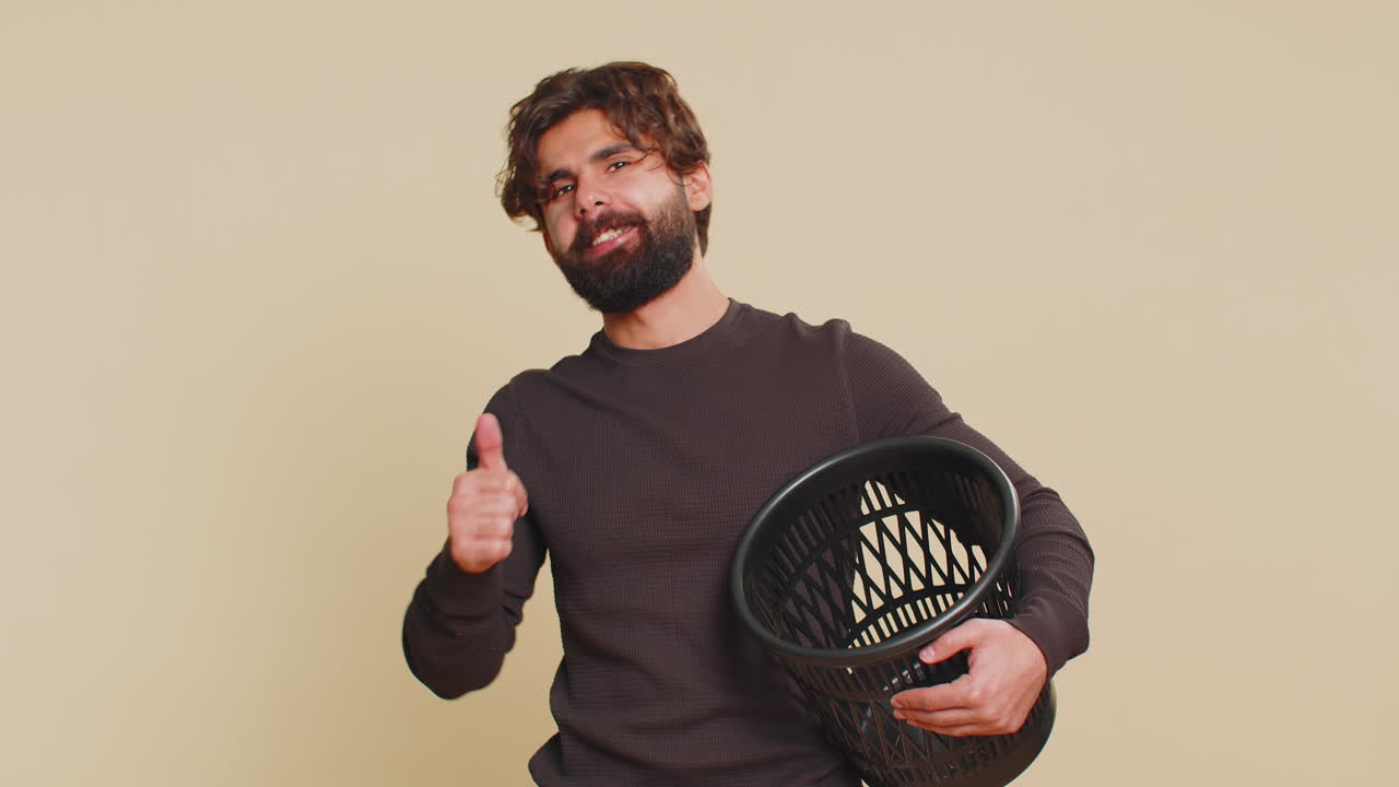 Indian young man taking off throwing out glasses into bin after laser treatment on beige background