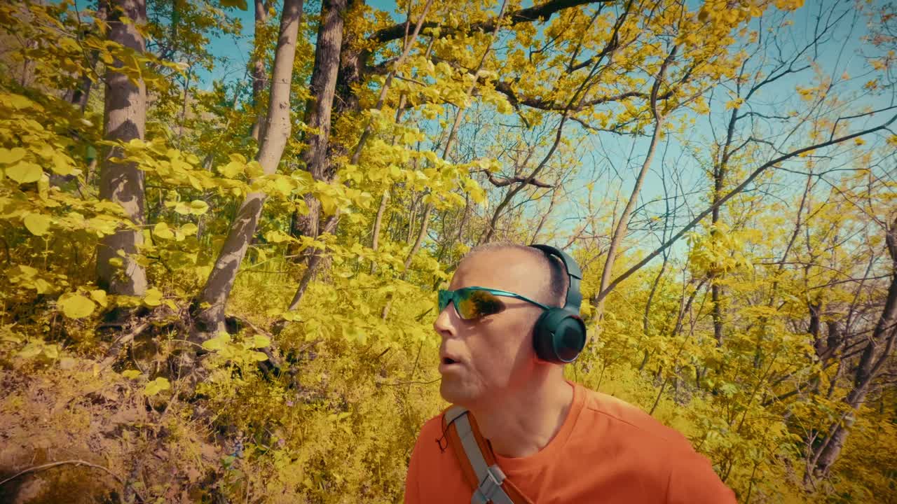 Un uomo maturo e rilassato sulla cinquantina ascolta musica in cuffia durante un'escursione. Concetto di sollievo per la salute mentale, riduzione dello stress e pace nella natura. Filmato 4K di alta qualità.