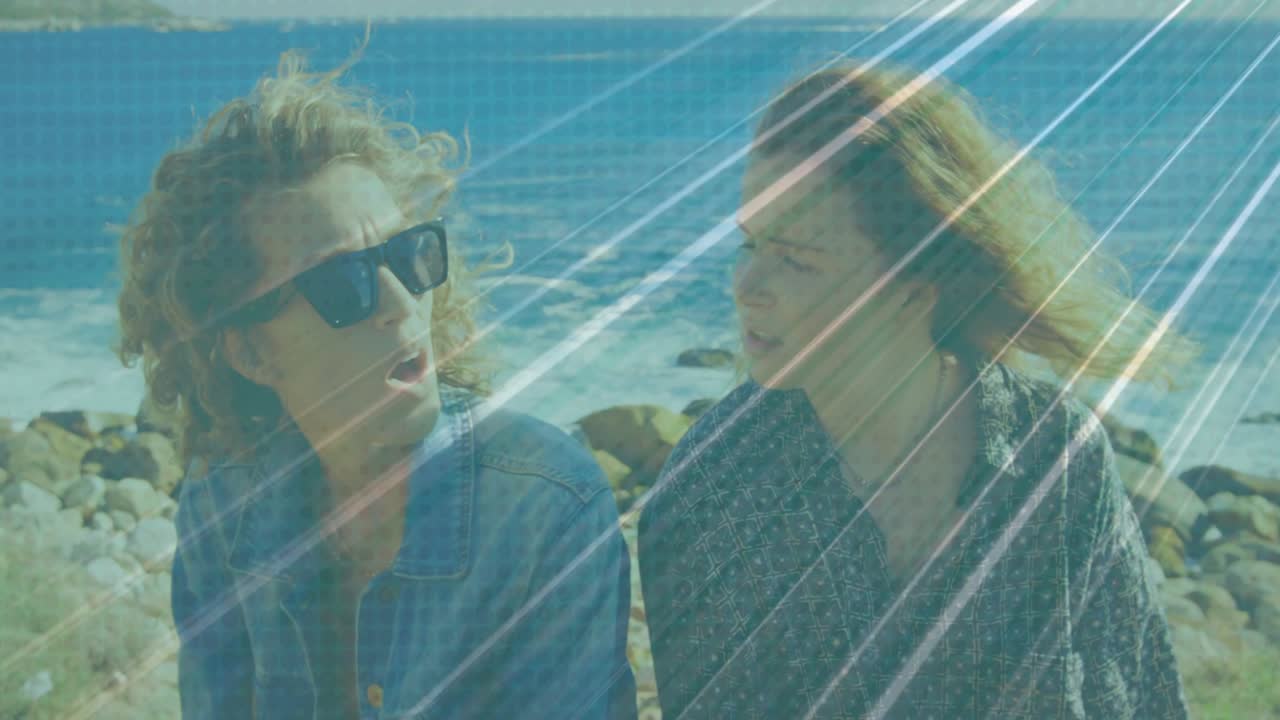 Due donne che si scambiano uno sguardo e poi si incontrano su una costa rocciosa, occhiali da sole, denim, con un bagliore dell'obiettivo che incornicia il viaggio.