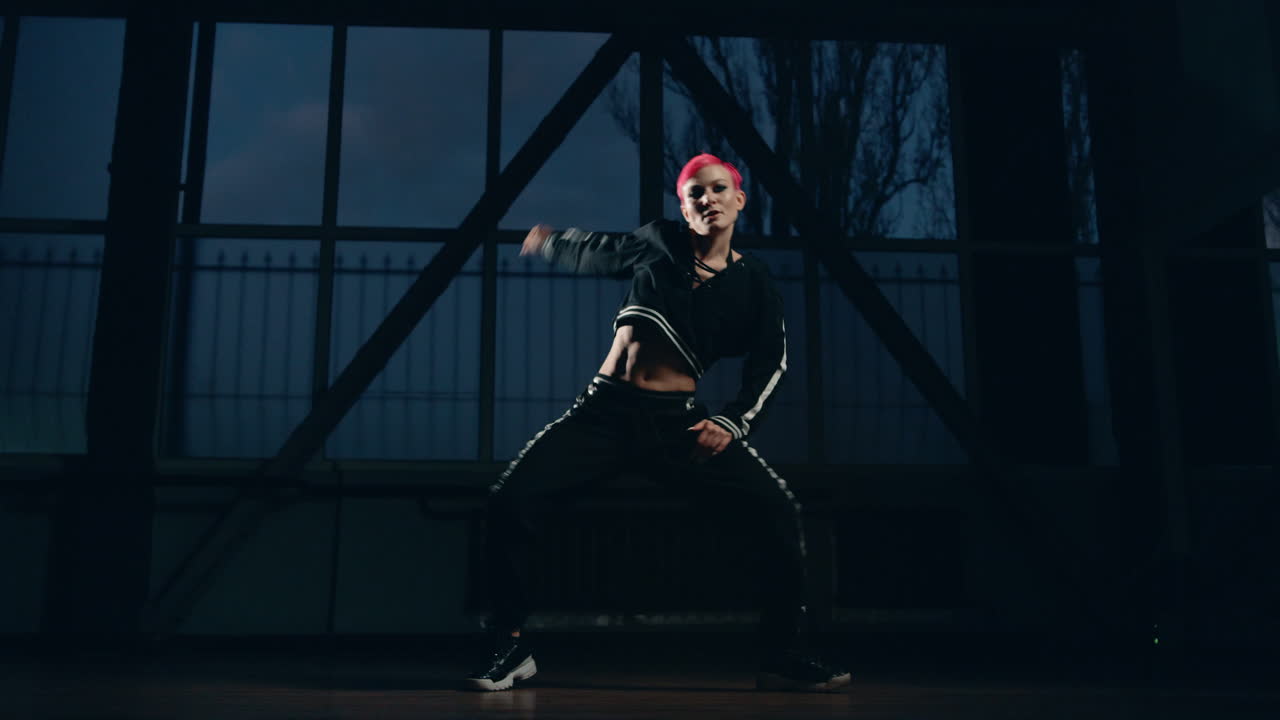 Young woman dancing hip hop in dark studio. Sportswear female dancer training.