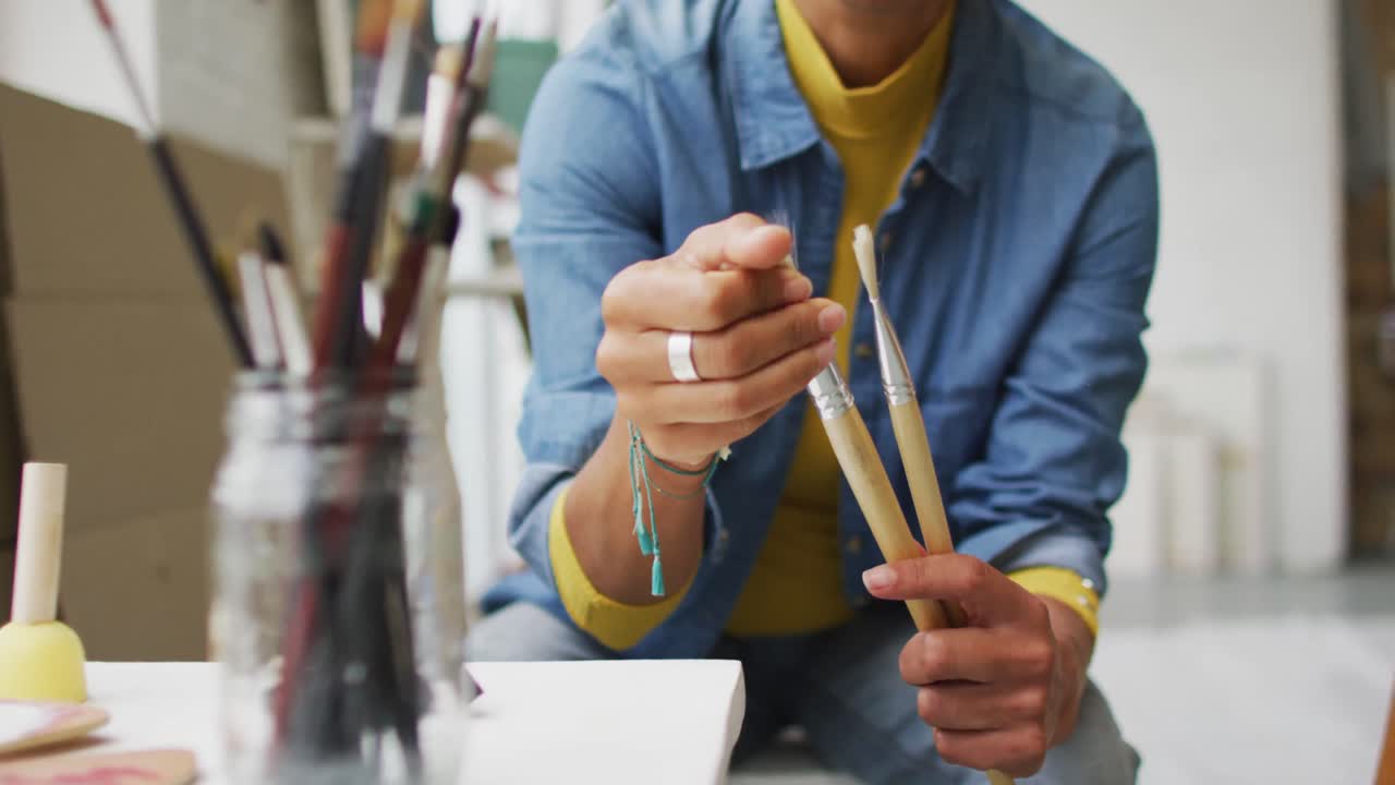 video de la sección media de una artista biracial en el estudio sosteniendo pinceles