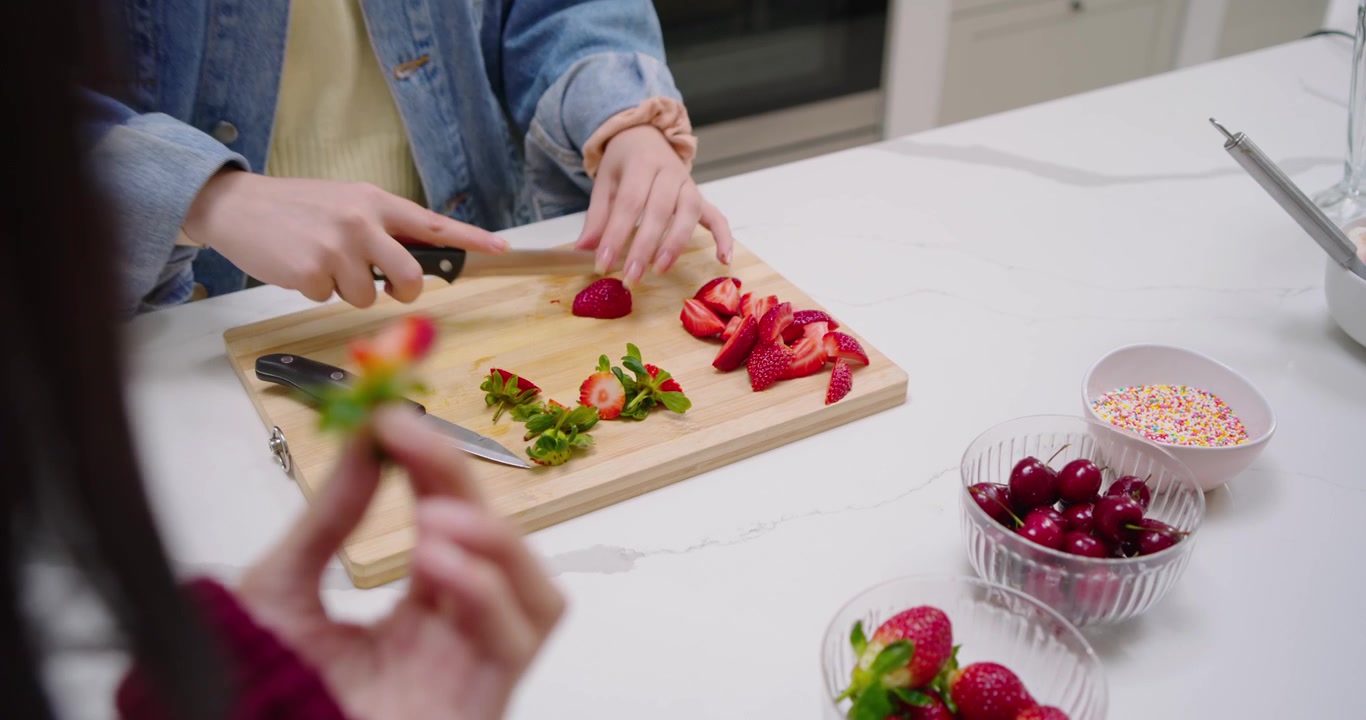 Diverse women, denim woman slicing strawberries on counter after placing berry for decorating