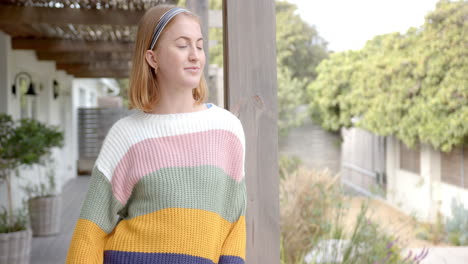 woman in colorful sweater standing on porch, looking away thoughtfully