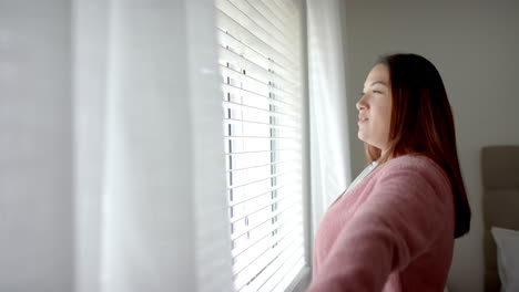 Mujer-Birracial-De-Talla-Grande-Dibujando-Cortinas,-Mirando-Por-La-Ventana-Del-Dormitorio,-Espacio-Para-Copiar,-Cámara-Lenta