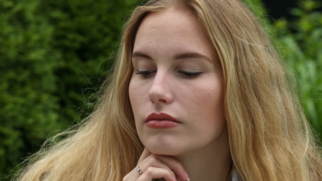 primer plano estático de la cara de una modelo rubia mientras descansa su barbilla en su mano pensando