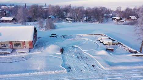 person blowing snow with gasoline equipment near farm building, drone flying close shot