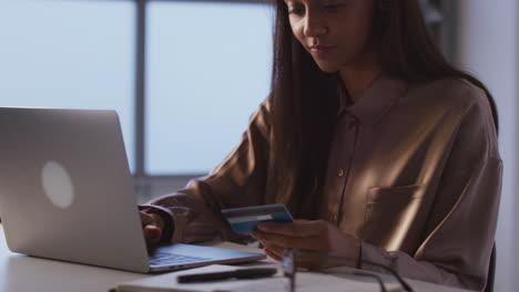 mujer de negocios trabajando hasta tarde en la computadora portátil en el escritorio en la oficina haciendo pagos en línea con tarjeta de crédito