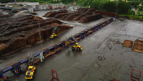 wheeled grapple loaders move logs from conveyor system at lumber yard