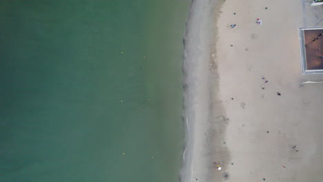 Coastal-Aerial-View-of-Gdynia-Orlowo-Sandy-Beach,-Top-Down-View-of-Clear-Calm-Green-Sea-Water-at-the-Seashore-and-People-Walking-on-Shore,-Summer-Holiday-Tourist-Destination,-Coast-Seascape