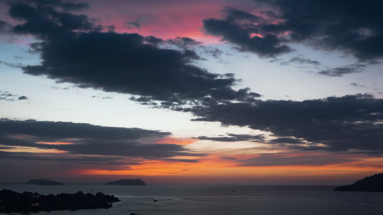 Aerial view of a dramatic colorful sunset sky with orange and pink clouds above the calm sea and silhouetted islands of the Kota Kinabalu waterfront