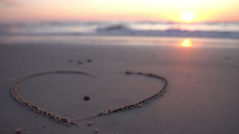 heart symbol drawn on sand against a backdrop of sunset over the sea