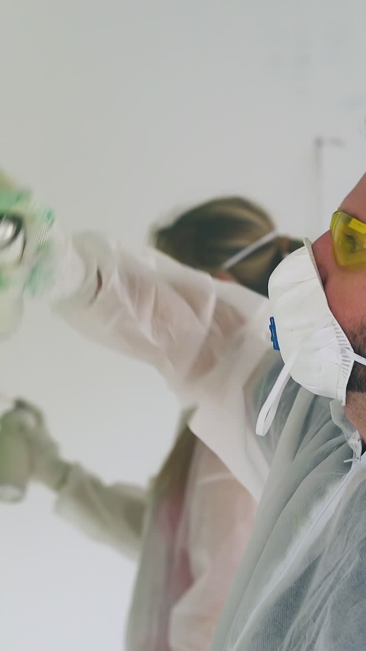guy in goggles and girlfriend in protective suits and masks paint white wall using bright sprays in light repairing room