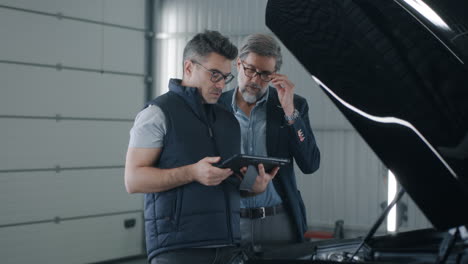 two men using a tablet to discuss car diagnostics in a garage