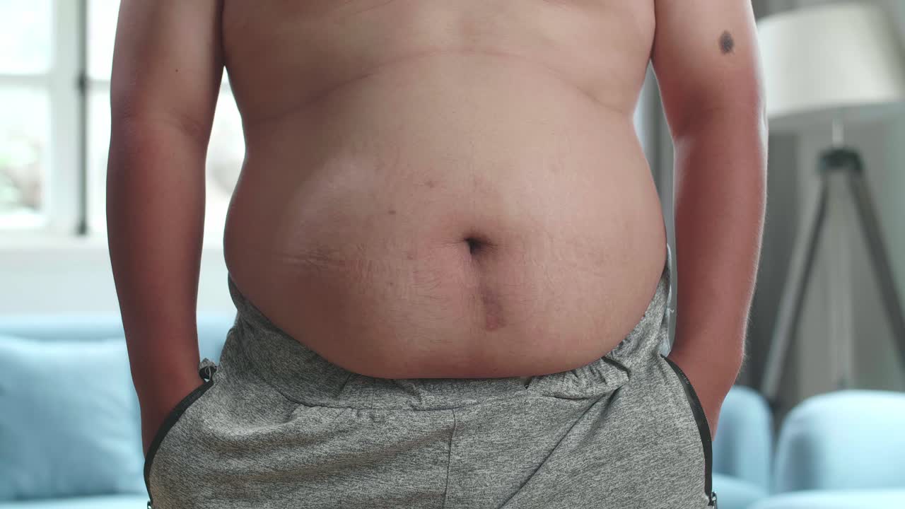 cerca de un hombre gordo con grasa en el vientre pone su mano en el bolsillo de los pantalones