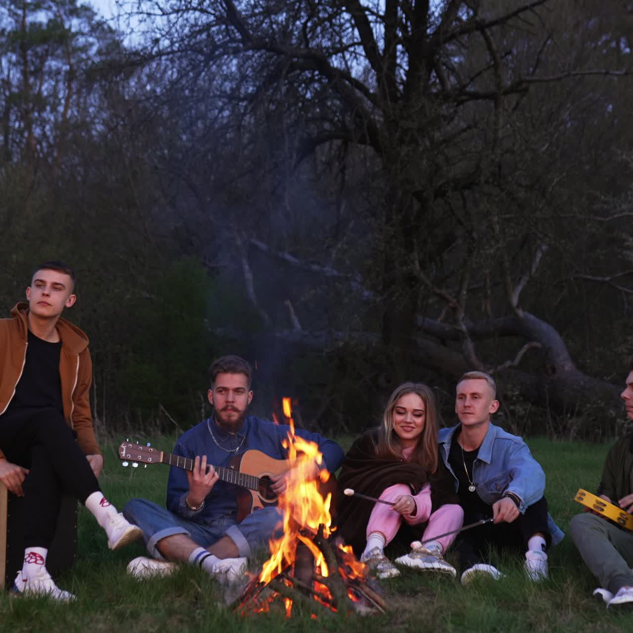 Traveling with friends and sitting near the campfire. Group of people outdoor sitting in the evening near the fire