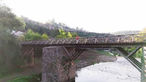 man walking on vladishki most with tsarevets fortress in background, zoom shot capturing medieval veliko tarnovo charm.
