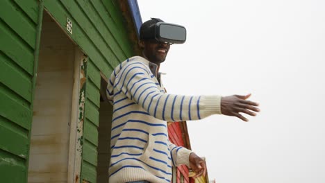 Vista-Lateral-De-Un-Joven-Negro-Haciendo-Gestos-Mientras-Usa-Auriculares-De-Realidad-Virtual-En-Una-Cabaña-En-La-Playa-4k