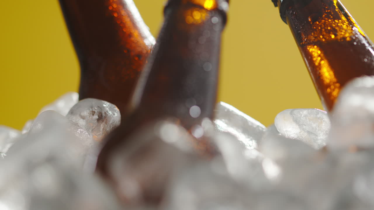 Close Up Of Glass Bottles Of Cold Beer Or Soft Drinks Chilling In Ice Filled Bucket Against Yellow Background
