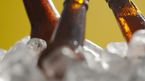 Close-Up-Of-Glass-Bottles-Of-Cold-Beer-Or-Soft-Drinks-Chilling-In-Ice-Filled-Bucket-Against-Yellow-Background