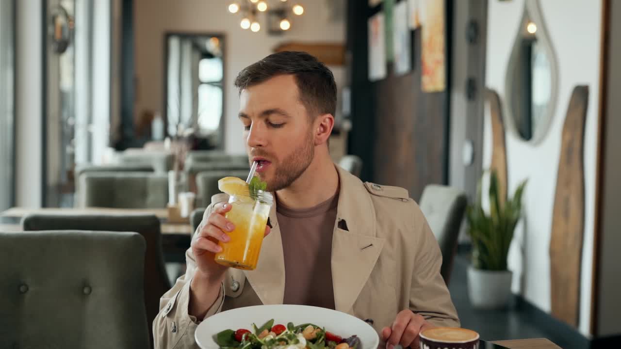 hombre alegre y elegante bebiendo un cóctel y sonriendo mientras se sienta en un café