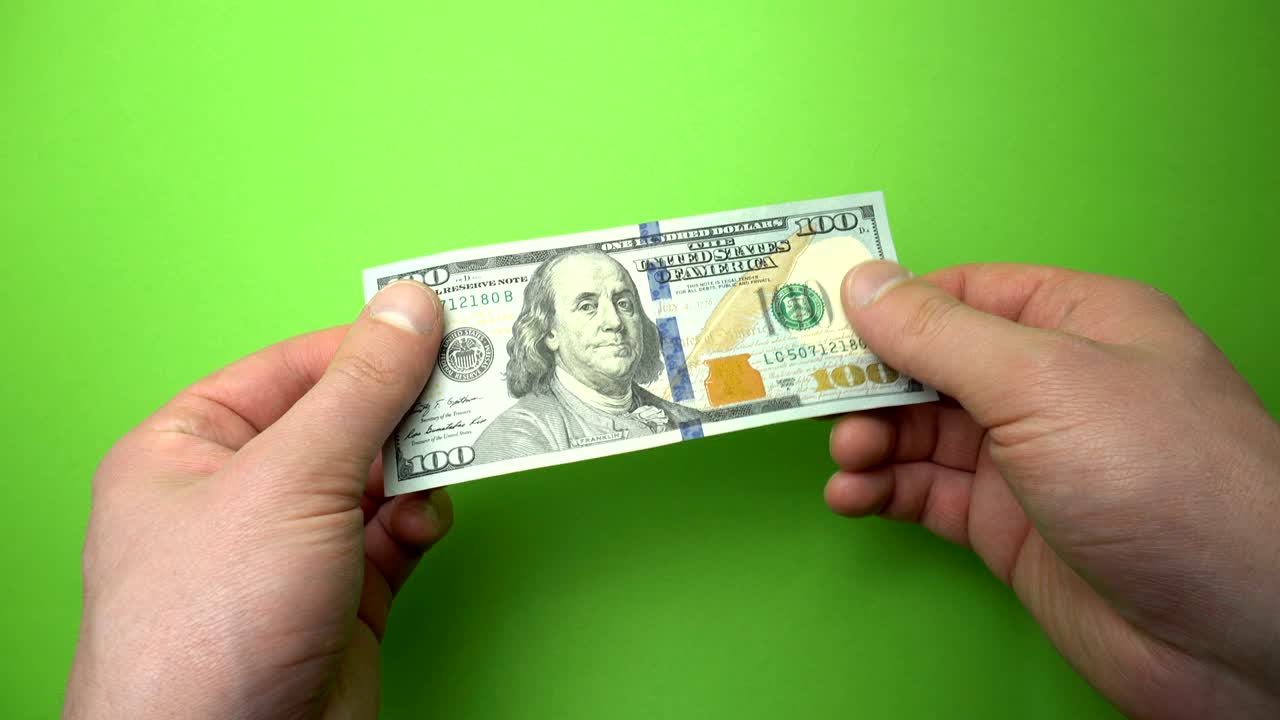 un billete de 100 dólares en la mano de un hombre cercano.