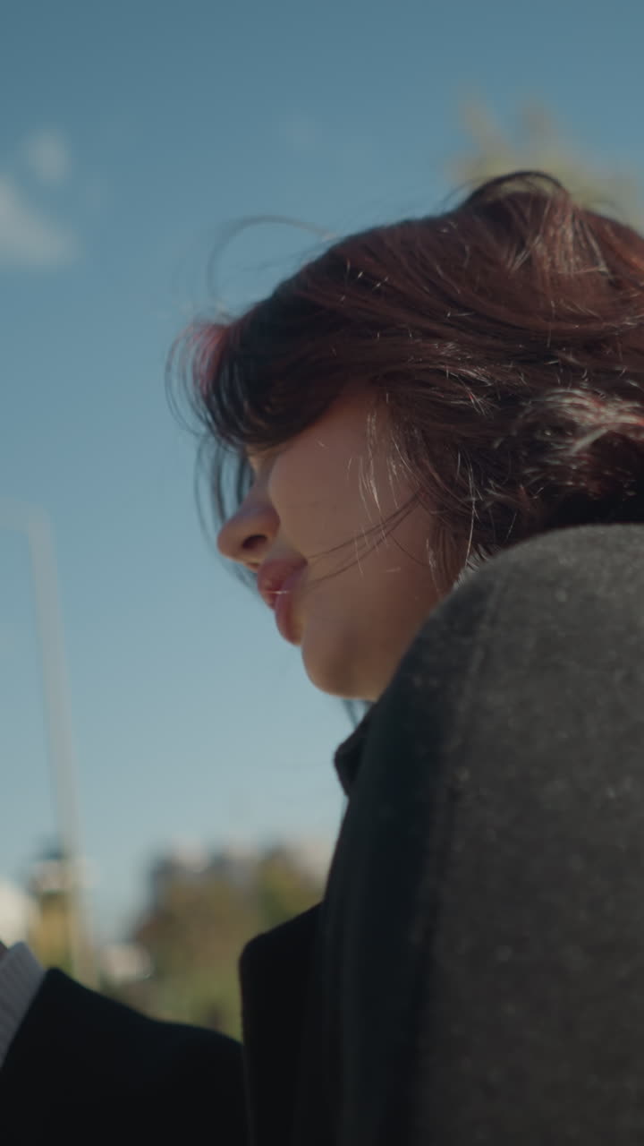 primer plano de una joven sonriendo mientras se balancea al aire libre, su cabello balanceándose con la brisa mientras lo ajusta, rodeado de vegetación en un parque soleado y brillante