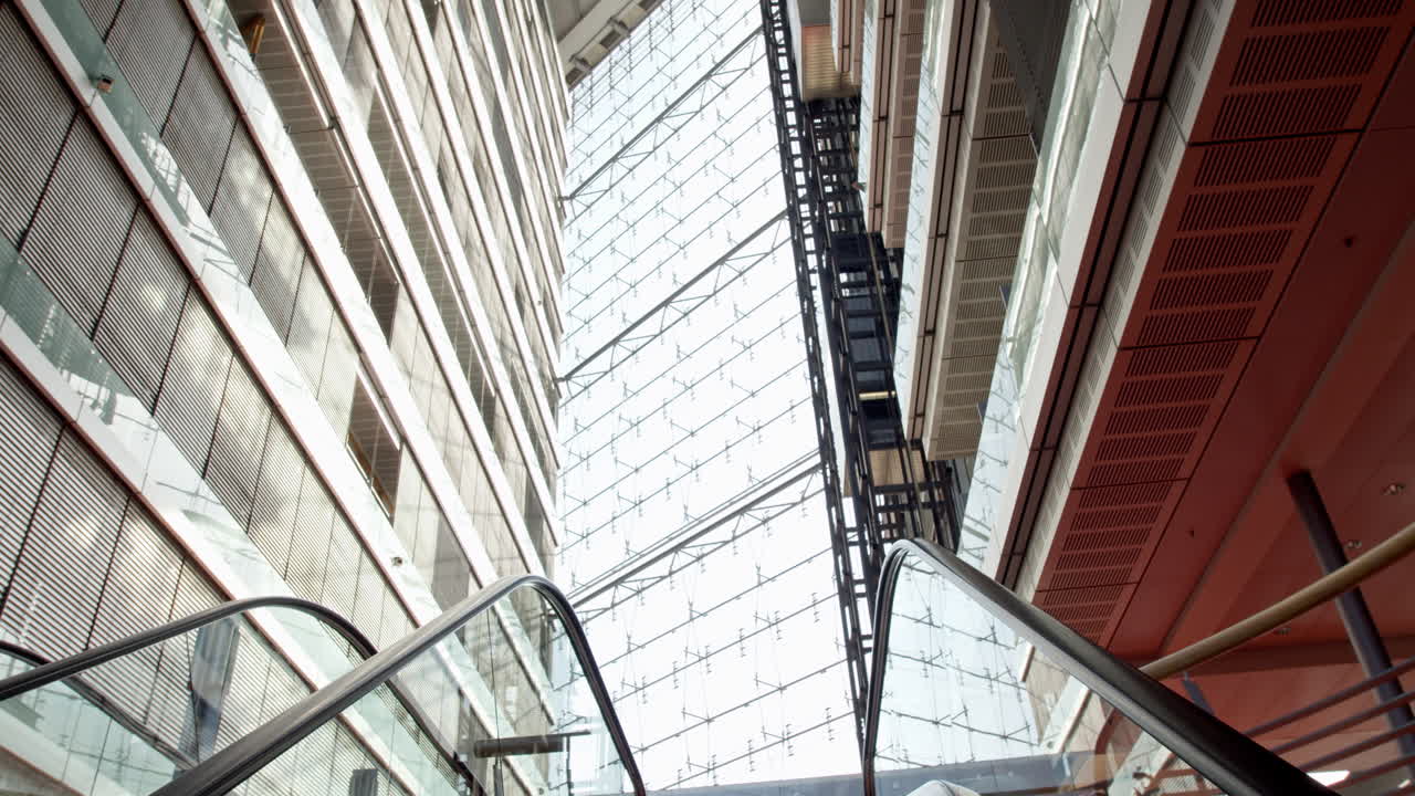 High-resolution video from D&uuml;sseldorf's Stadttor, showcasing a camera ascending an escalator beside an elevator, with abundant glass architecture enhancing the dynamic scene