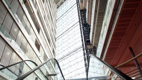 High-resolution-video-from-Düsseldorf's-Stadttor,-showcasing-a-camera-ascending-an-escalator-beside-an-elevator,-with-abundant-glass-architecture-enhancing-the-dynamic-scene