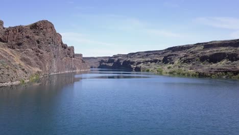 low scablands aerial: tall rock cliffs surround vivid blue deep lake