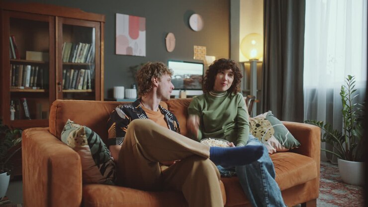 Young Couple Relaxing on Sofa, Eating Popcorn and Watching TV at Home