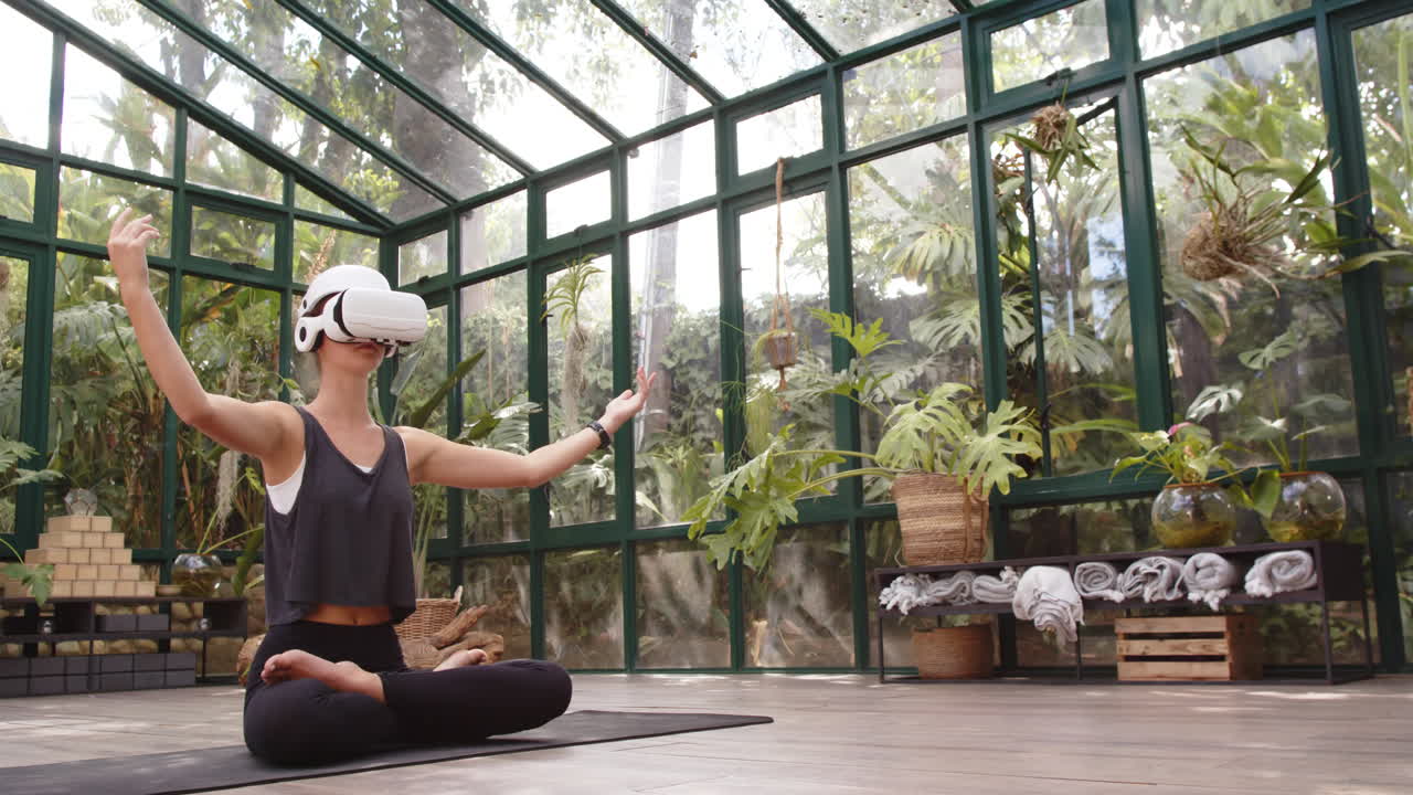 Yogande kvinna bär VR-headset i glashus, mediterar på matta, med plats för text.