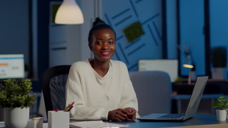 Business-black-woman-looking-at-camera-smiling-raising-head-from-laptop