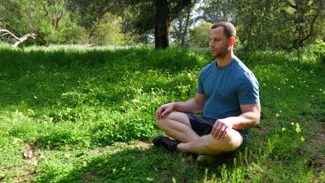 a man sitting in a meditation pose in a green sunny forest practicing deep breathing exercises to reduce stress and train mindfulness slow motion