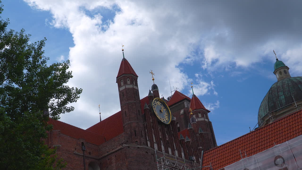 Close-up of St. Catherine’s Church clock tower against partly cloudy sky in Gdańsk